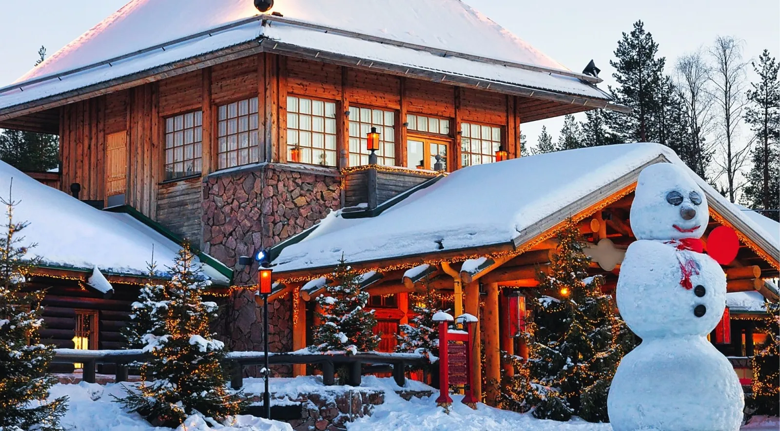 Illuminated wooden lodge and snowman at Santa Claus Village at dusk