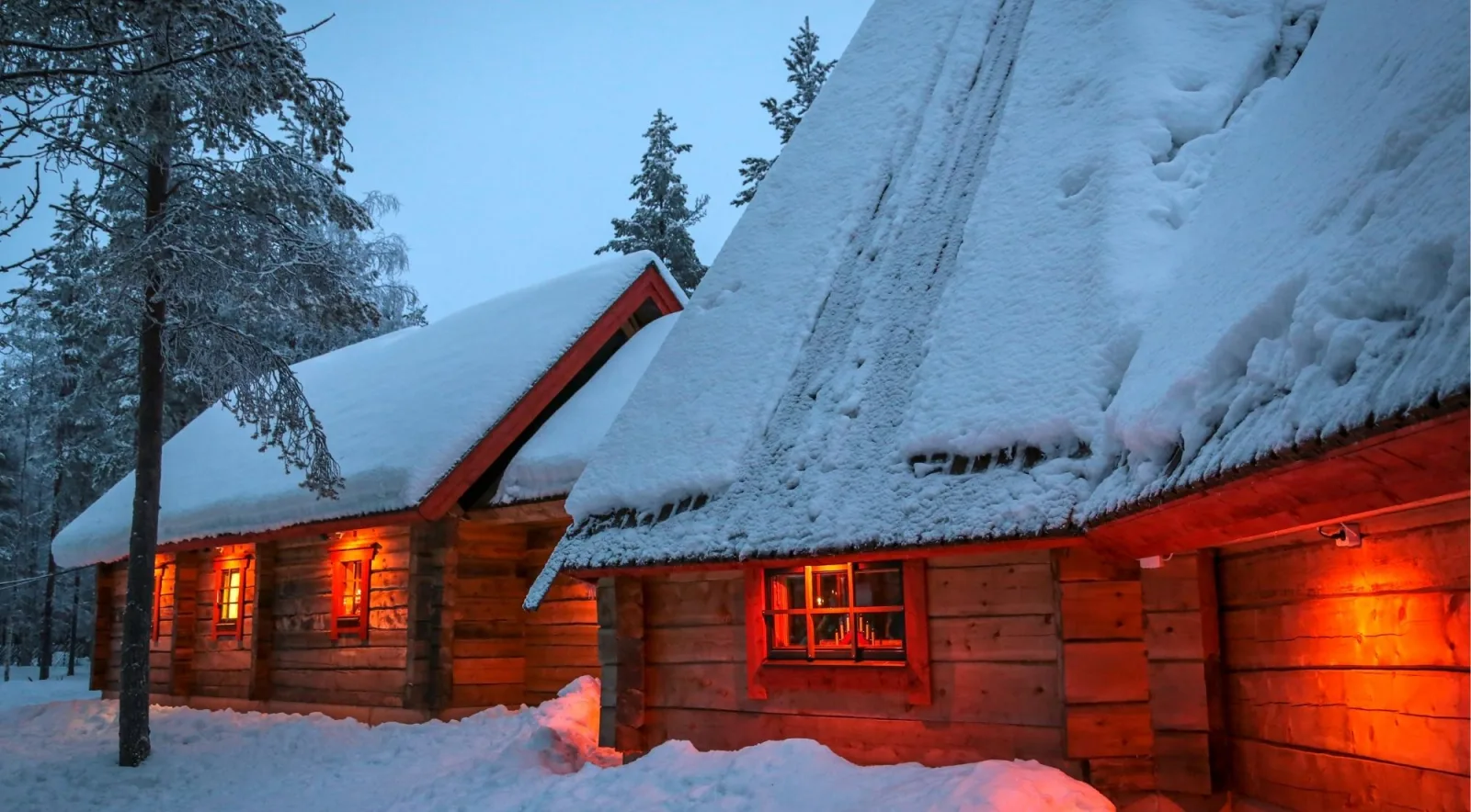Snow-laden log cabins glowing with warm window light at Arctic twilight